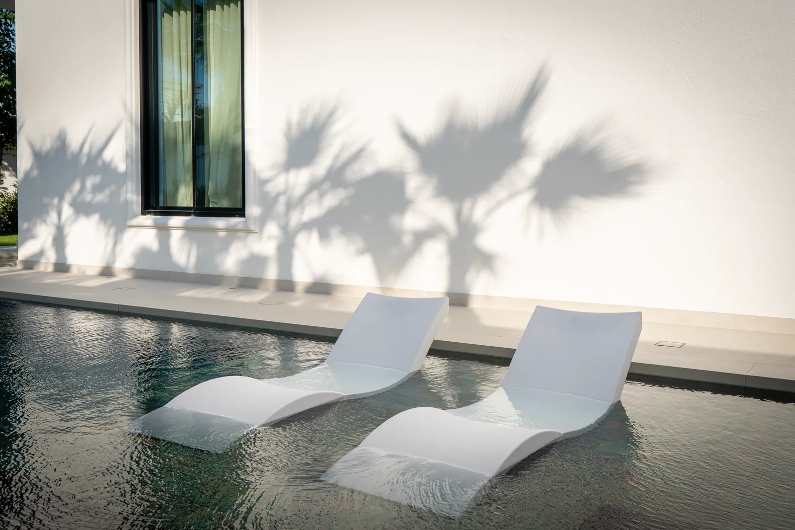 Loungers on the pool shelf with palm shadows across the wall
