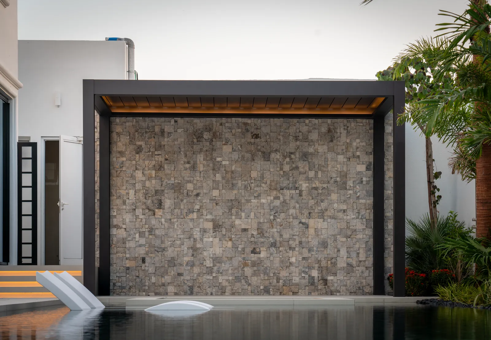 The stone water-feature wall mirrored in the pool at dusk