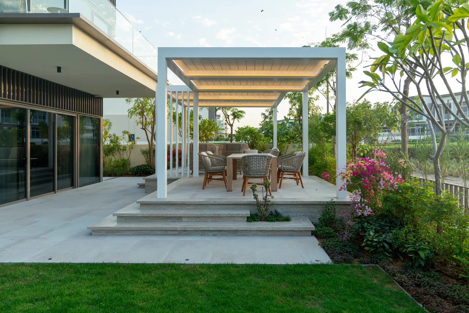 White pergola and outdoor dining seen across the lawn